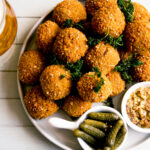 Een bord met biologische bitterballen van Royal Spelt, geserveerd met grove mosterd en augurkjes, naast een glas bier. Ambachtelijke spelt-snacks met knapperige korst, ideaal voor horeca en foodservice.