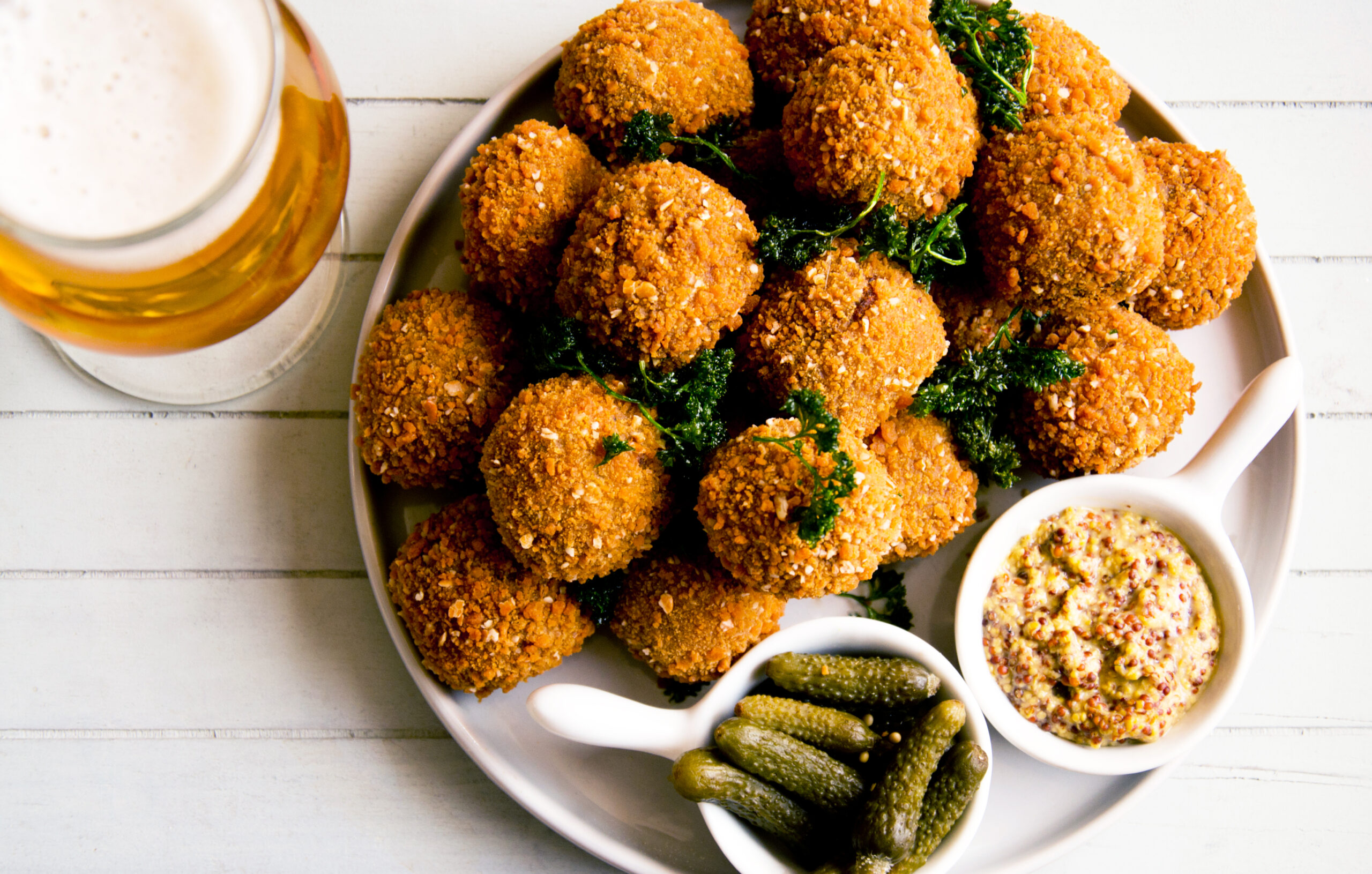 Een bord met biologische bitterballen van Royal Spelt, geserveerd met grove mosterd en augurkjes, naast een glas bier. Ambachtelijke spelt-snacks met knapperige korst, ideaal voor horeca en foodservice.